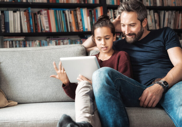 happy father and daughter having fun with digital tablet on couch